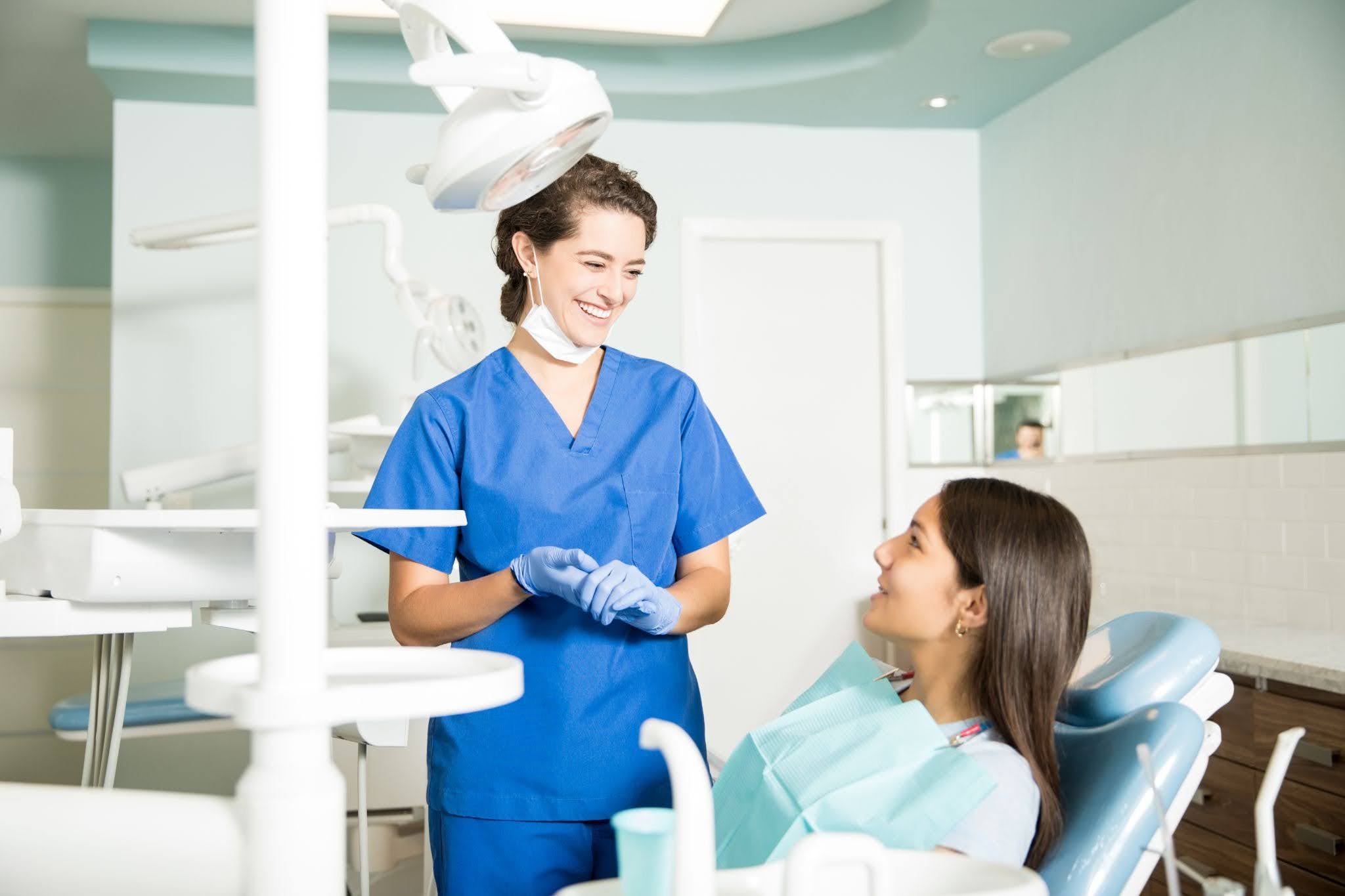 Smiling dentist speaking with a new patient seated in a modern dental treatment room.